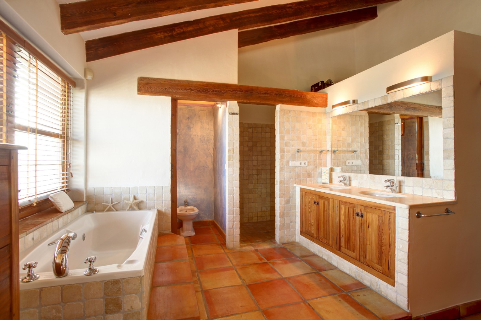 Rustic bathroom featuring exposed wooden beams, terracotta flooring, and a built-in bathtub. The double vanity includes mobila wood cabinetry, marble countertops, and stone tile accents.