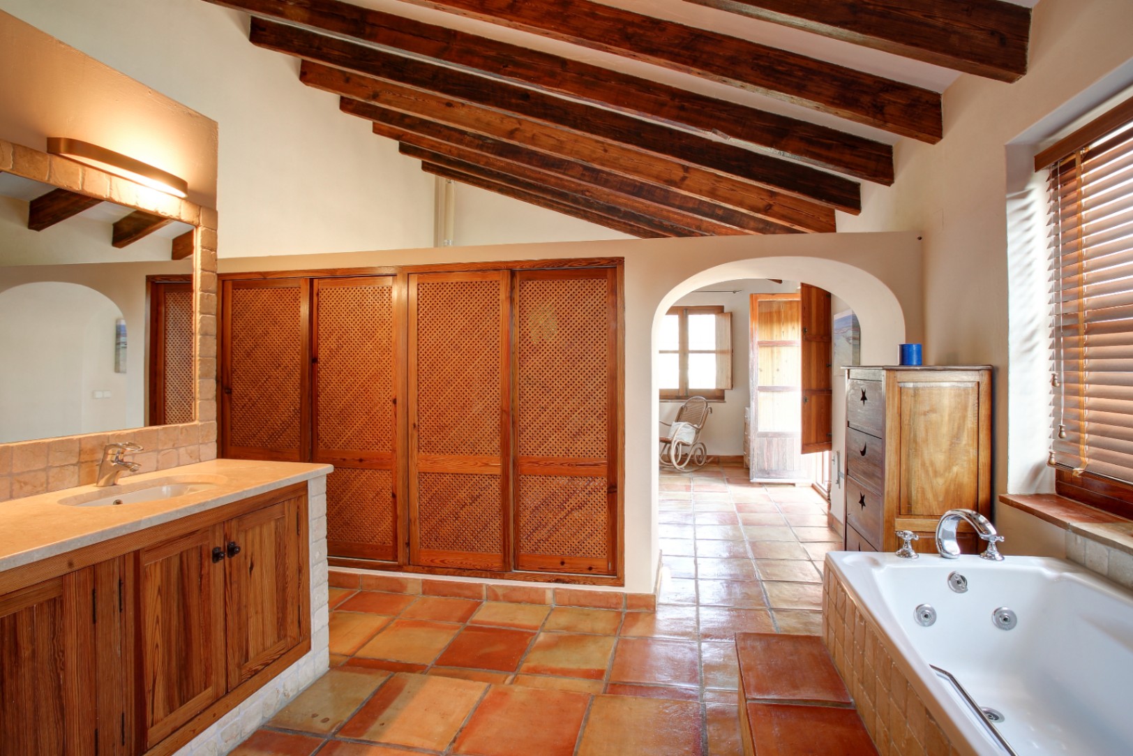 Rustic bathroom featuring exposed wooden beams, terracotta flooring, and a hydromassage tub. Includes custom lattice-door wardrobes and a marble-topped vanity.