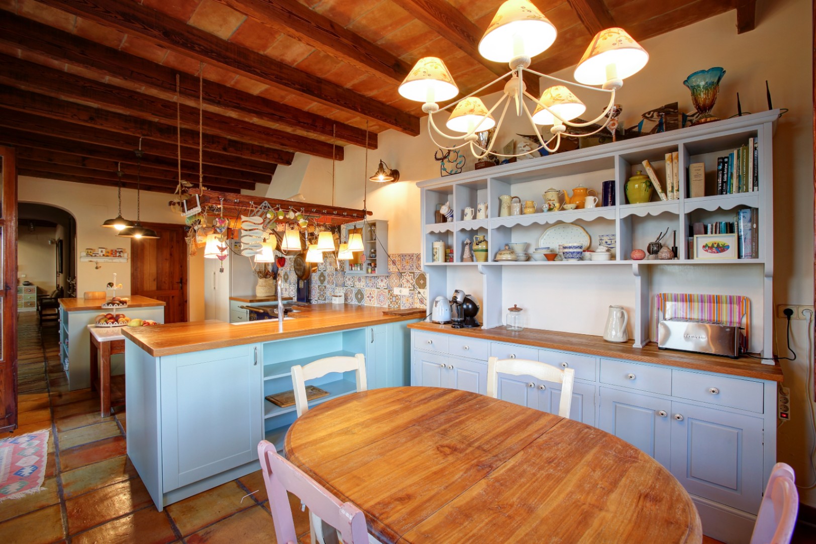 Rustic kitchen featuring light blue cabinetry, solid wood countertops, and exposed beam ceilings. The space includes a dining area with traditional terracotta flooring.