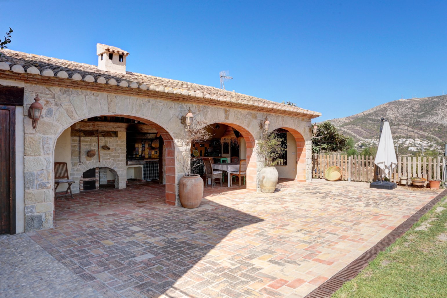 Rustic porch featuring stone arches, terracotta flooring, and a traditional built-in barbecue area overlooking the mountain landscape.