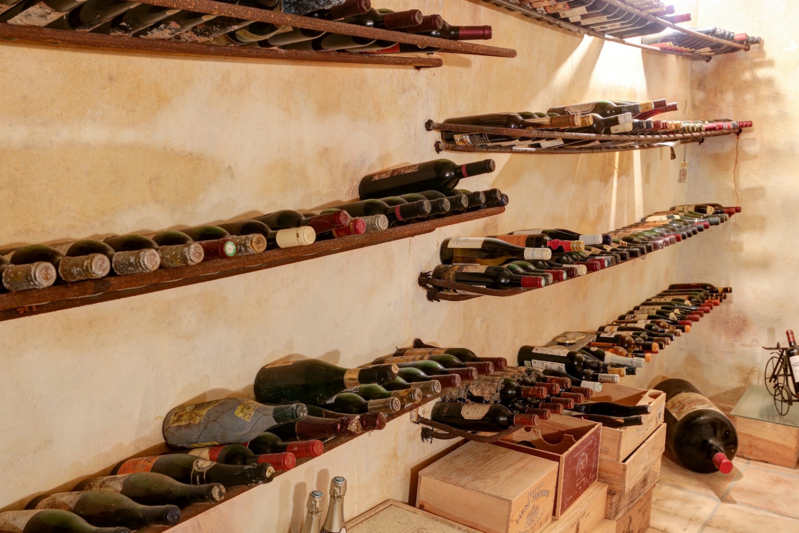 Rustic wine cellar featuring aged textured walls, wrought iron bottle racks, and authentic wooden crates for professional wine storage.