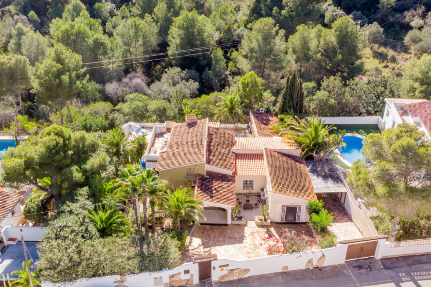 Aerial view of the villa showcasing its Mediterranean architecture with terracotta roofs, surrounded by a protected green zone and mature palm trees for total privacy.