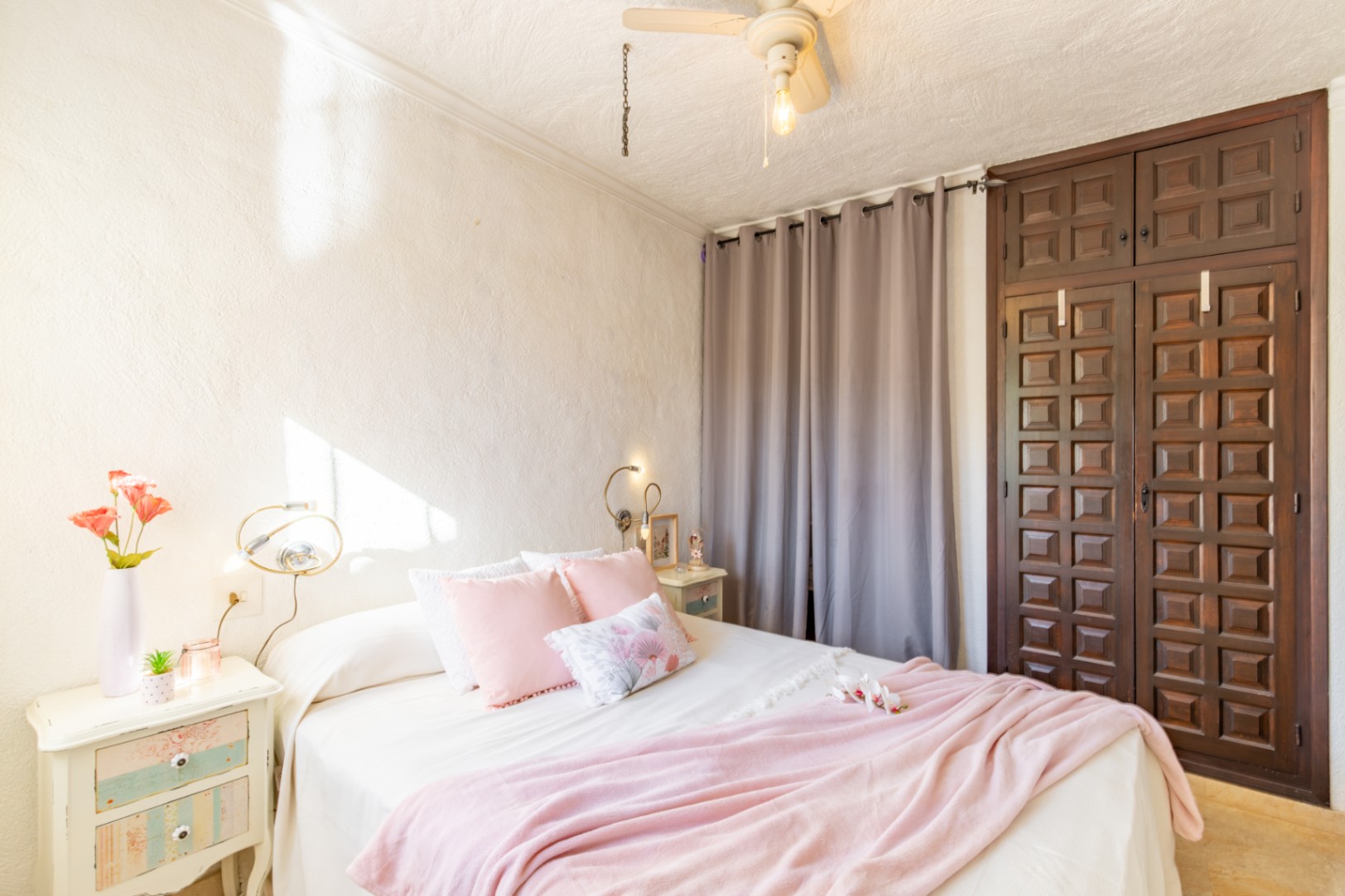 Bedroom featuring a dark wood built-in wardrobe with traditional paneling, textured white walls, and a ceiling fan. Natural light illuminates the space.