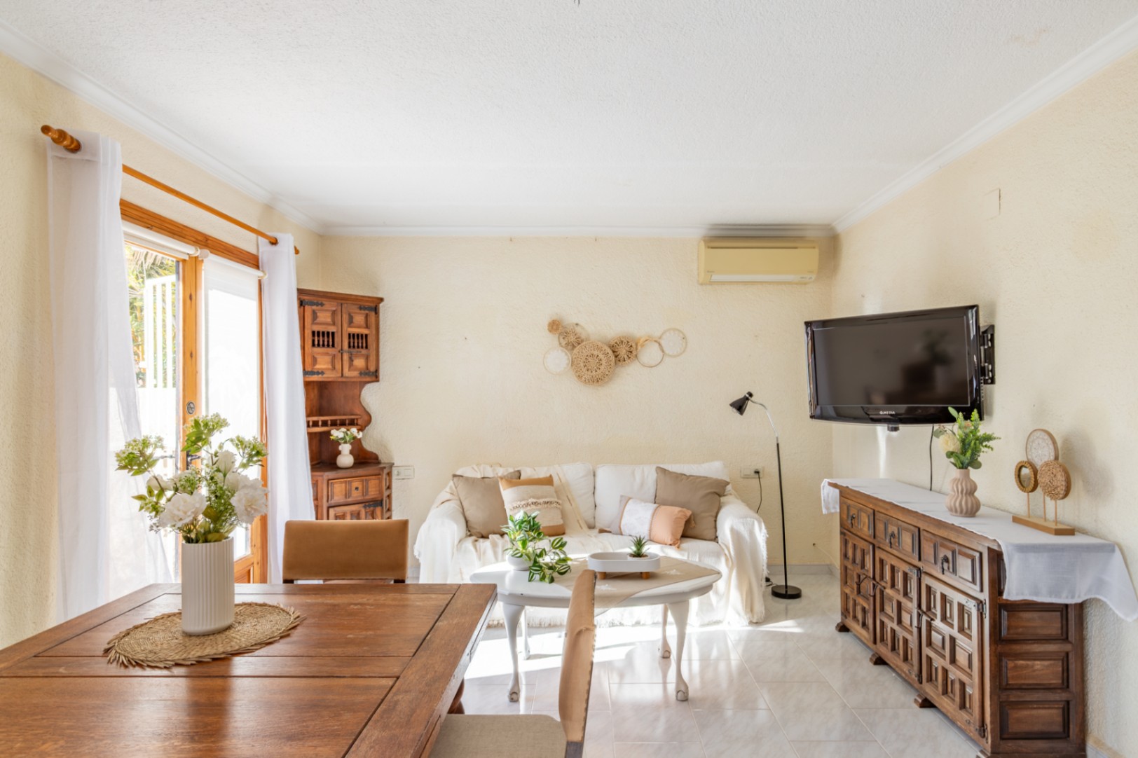 Bright living and dining area featuring rustic wooden furniture, ceramic tile flooring, and a glass door providing natural light and outdoor access.