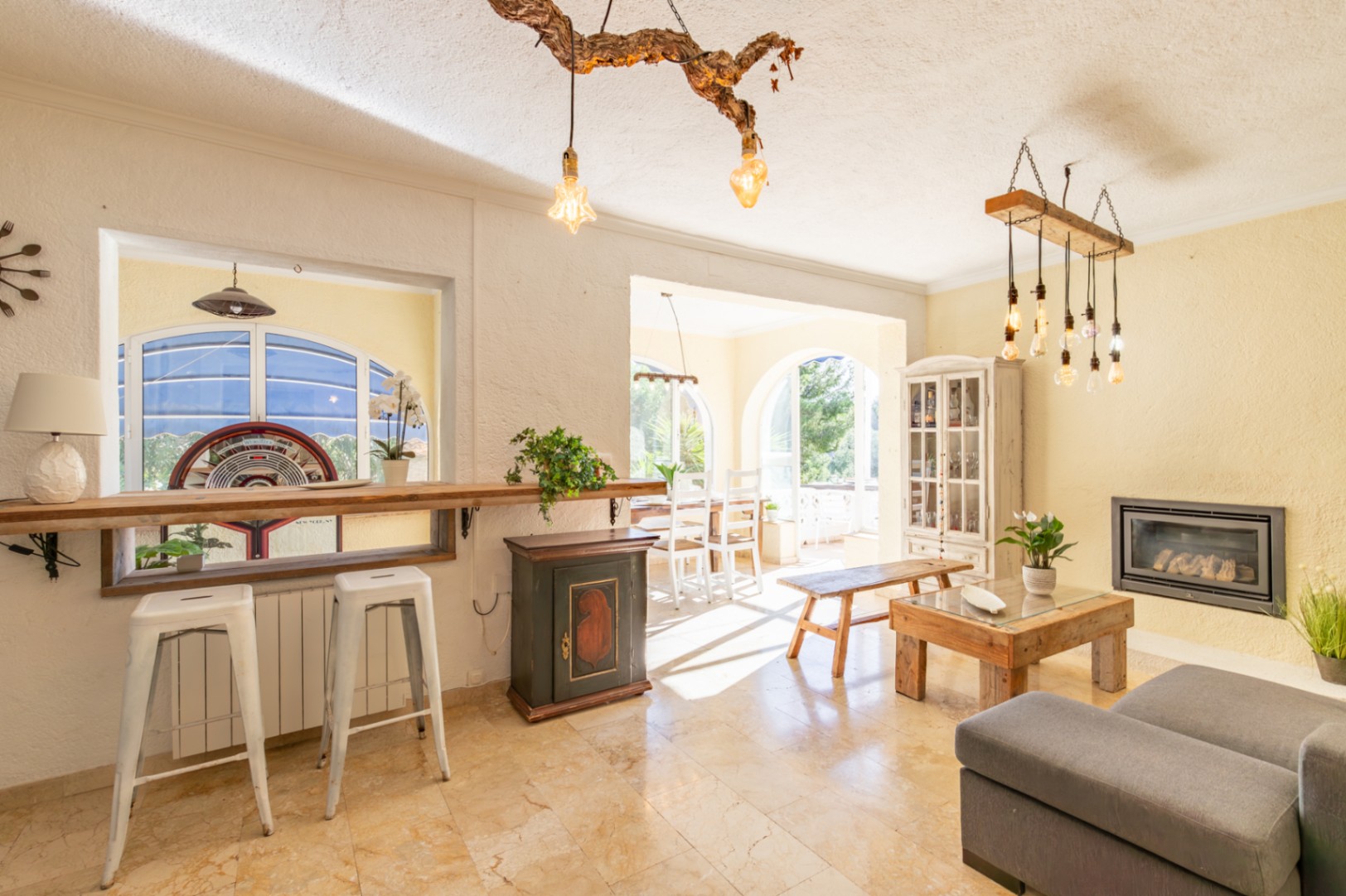 Bright living area featuring marble floors, a built-in fireplace, and a rustic bar. Unique branch-style lighting connects the lounge to the sunlit dining space.