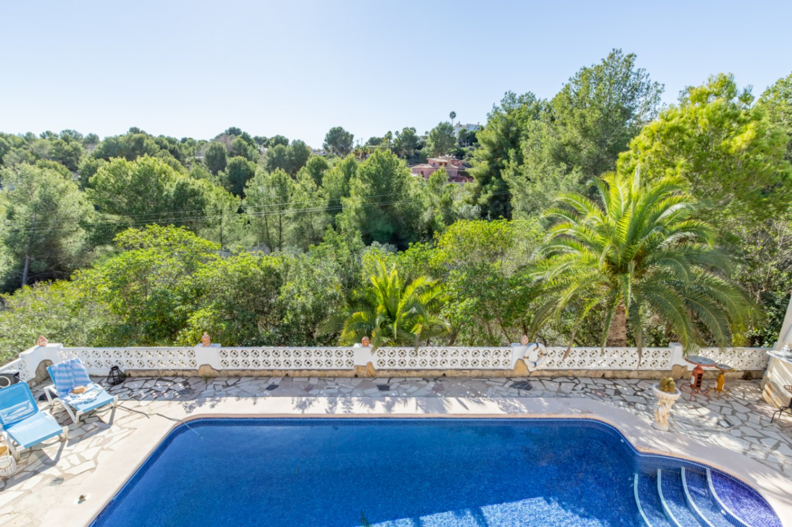 Elevated view of the 42 m² swimming pool and natural stone terrace, featuring a white decorative balustrade and unobstructed views of the adjacent protected green zone.