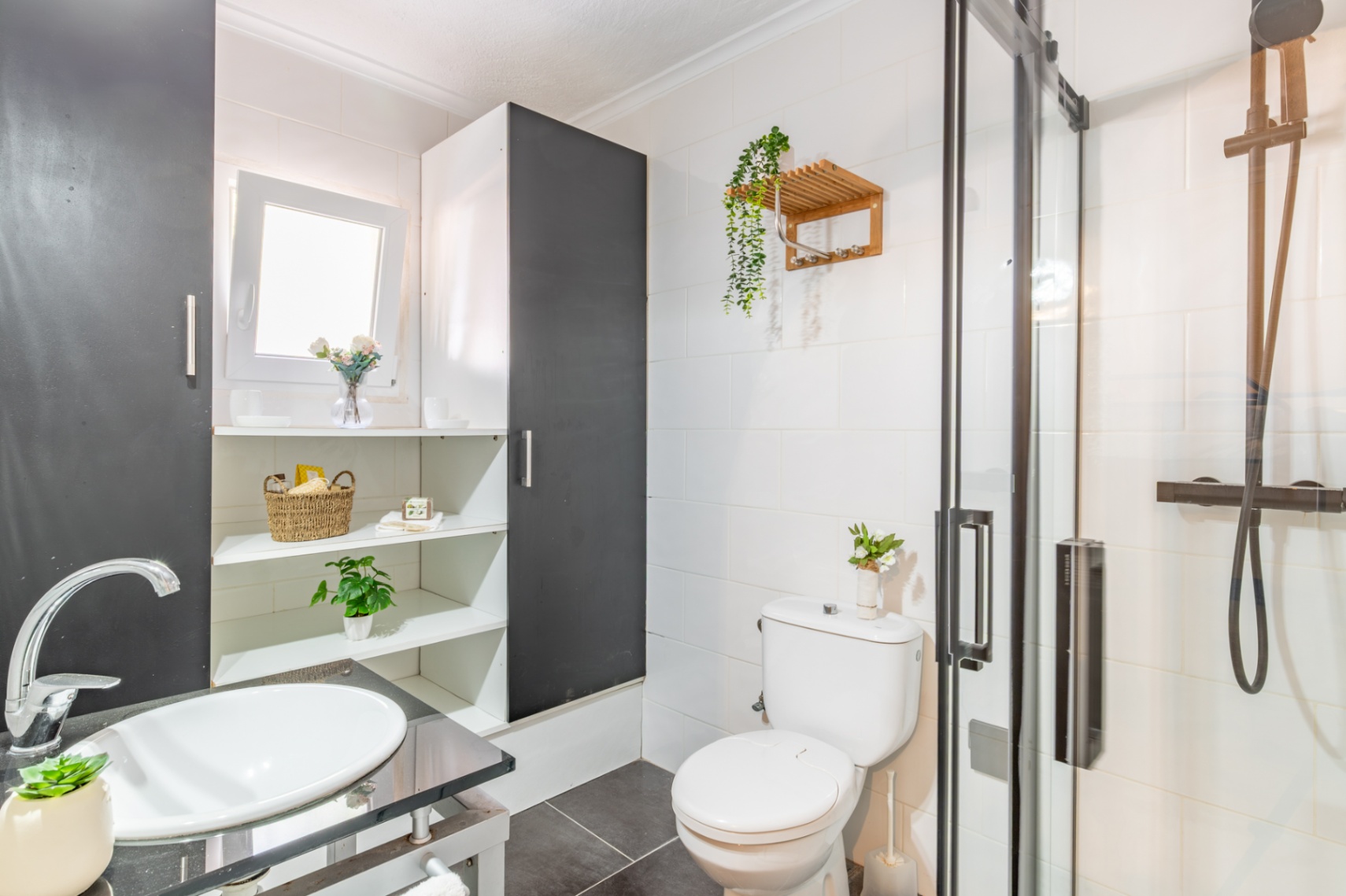 Functional bathroom featuring a walk-in glass shower with black fixtures. It includes a white vessel sink on a dark countertop and integrated shelving.