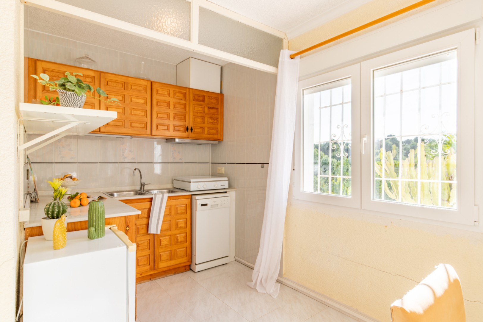 Functional kitchenette in the independent apartment featuring wooden cabinetry, white appliances, and a large window with natural light.