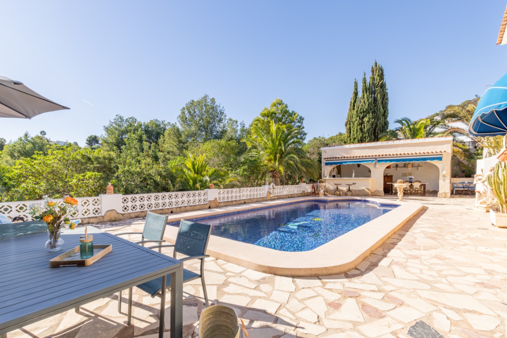 Outdoor area featuring a 42 sqm pool, natural stone terrace, and covered summer kitchen, bordered by mature greenery and views of the protected zone.