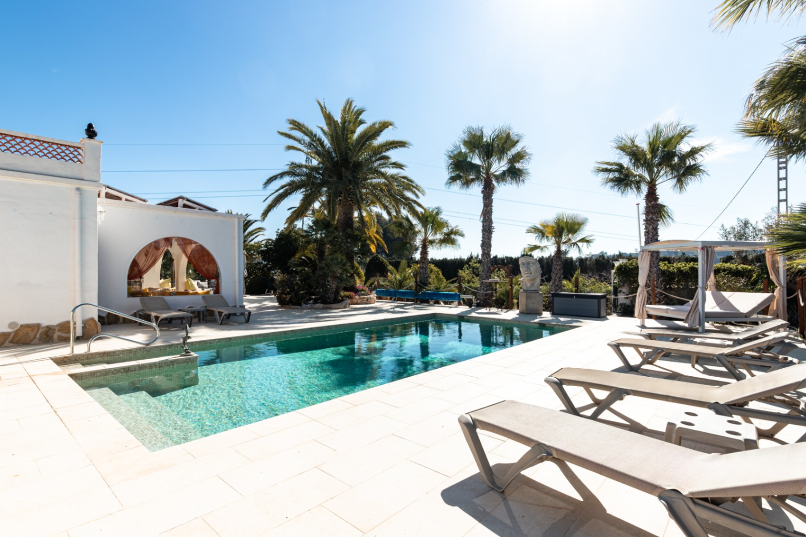 A 9.5m x 5m swimming pool surrounded by a light-tiled terrace, featuring sun loungers, a private cabana, and mature palm trees.