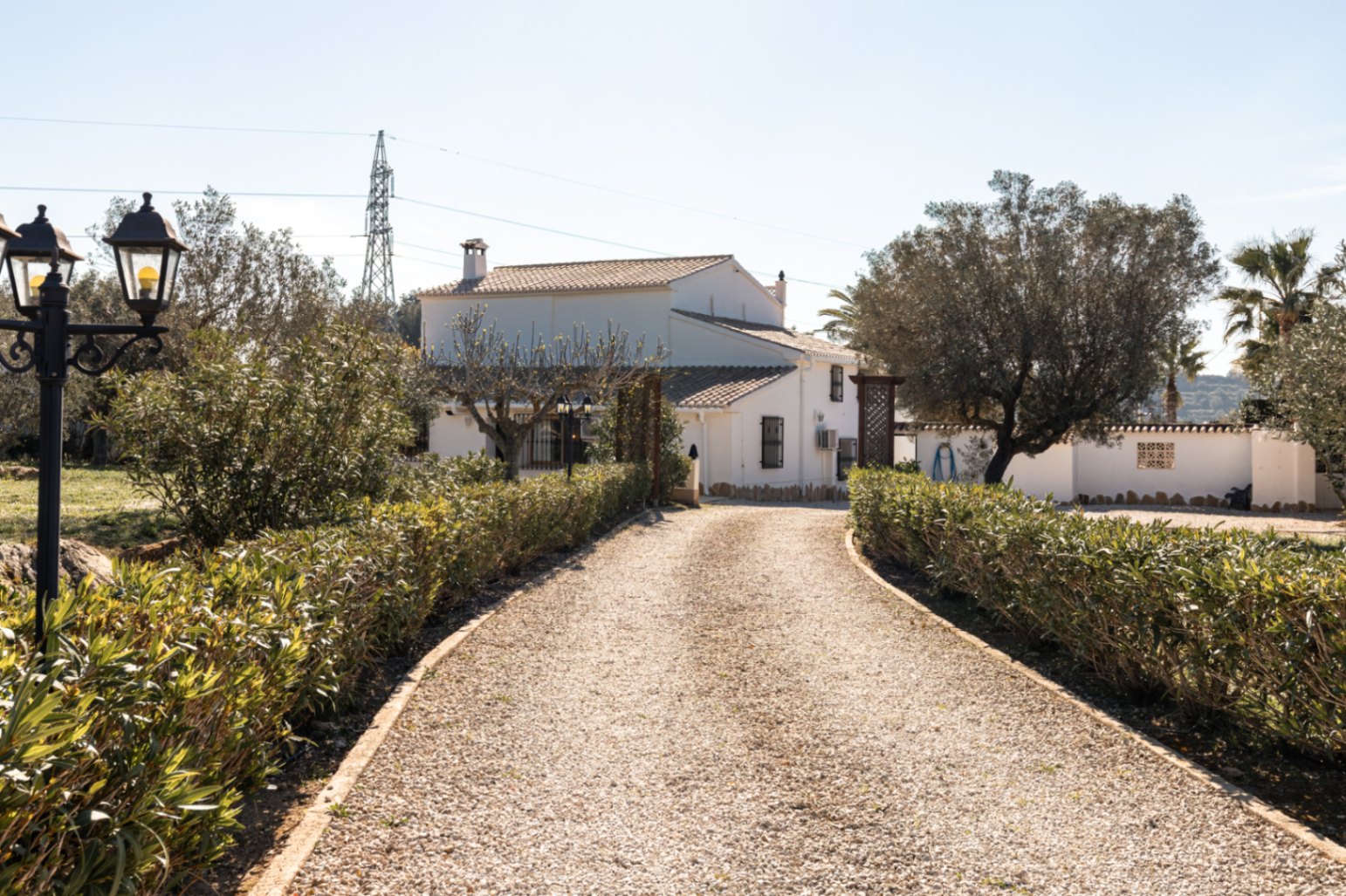 A gravel driveway bordered by manicured hedges leads to the white-washed facade of the finca, showcasing traditional Mediterranean architecture and mature trees.