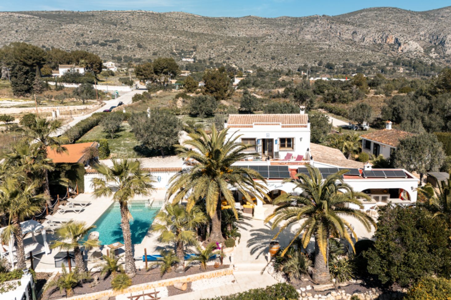 Aerial view of the property showcasing the private pool, rooftop solar panels, and landscaped Mediterranean gardens with mountain views.