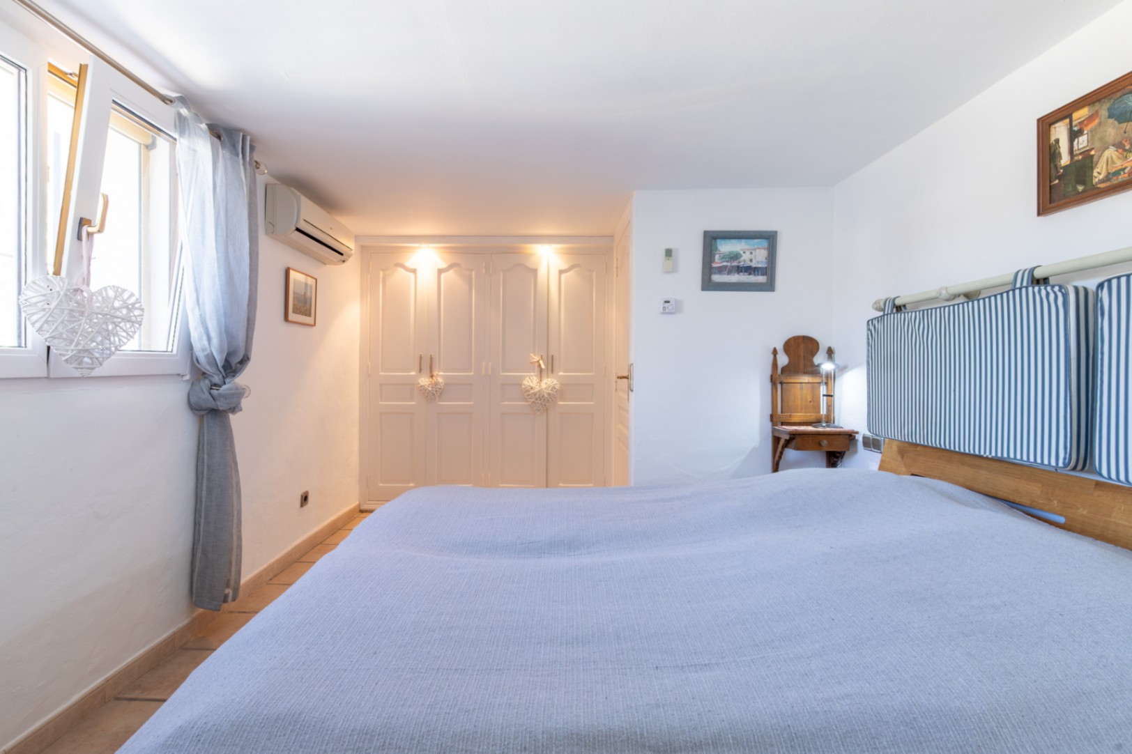 Bedroom featuring built-in white wardrobes with integrated lighting, air conditioning, and a bed with striped textile cushions against white walls.