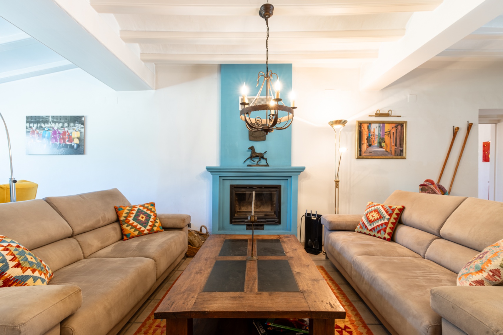 Bright living area featuring white beamed ceilings, a vibrant blue fireplace, and comfortable sofas arranged around a rustic wood and slate coffee table.