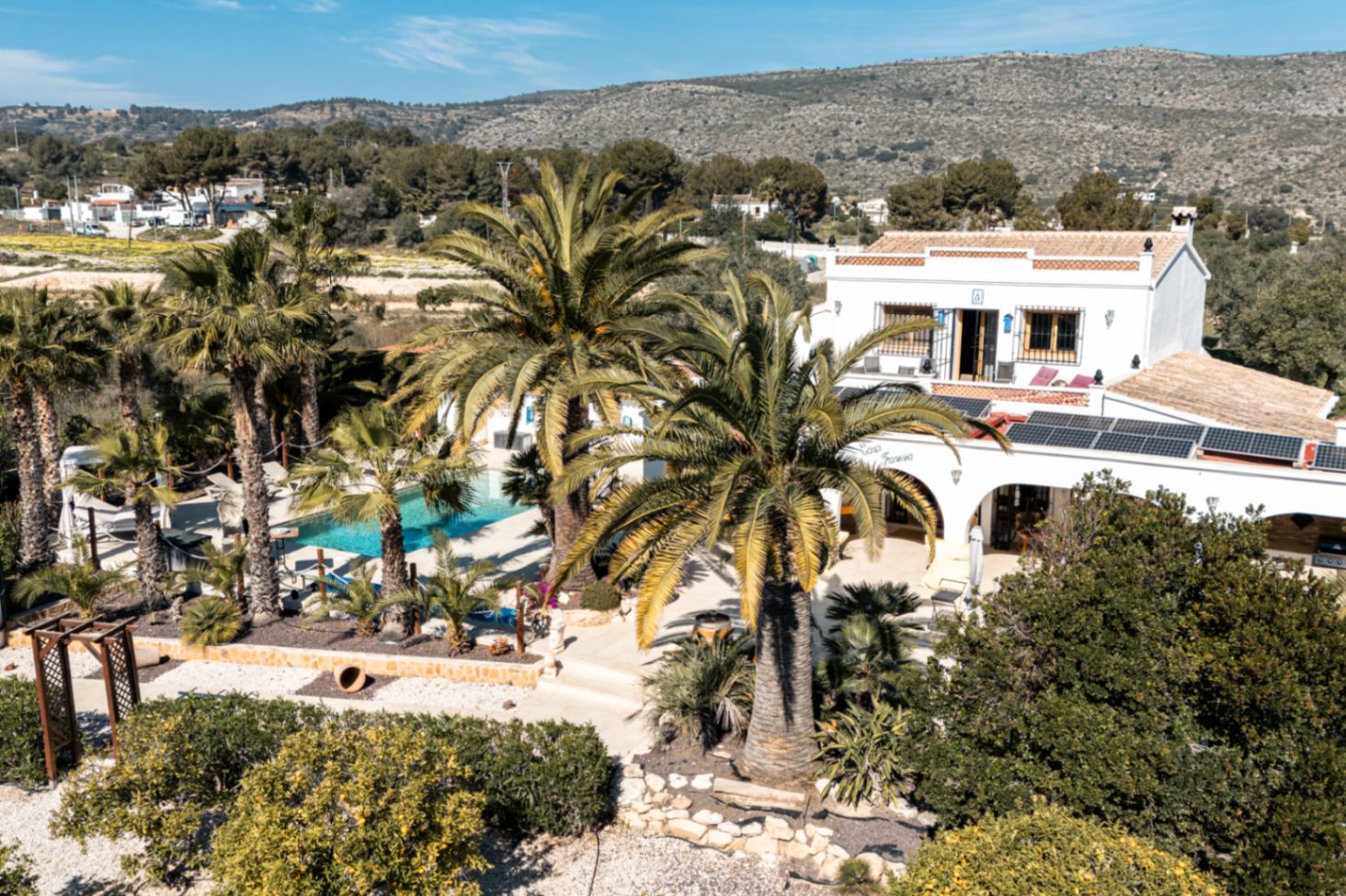 Elevated view of the finca showcasing the solar panel installation, the private swimming pool framed by mature palms, and the traditional white architecture.