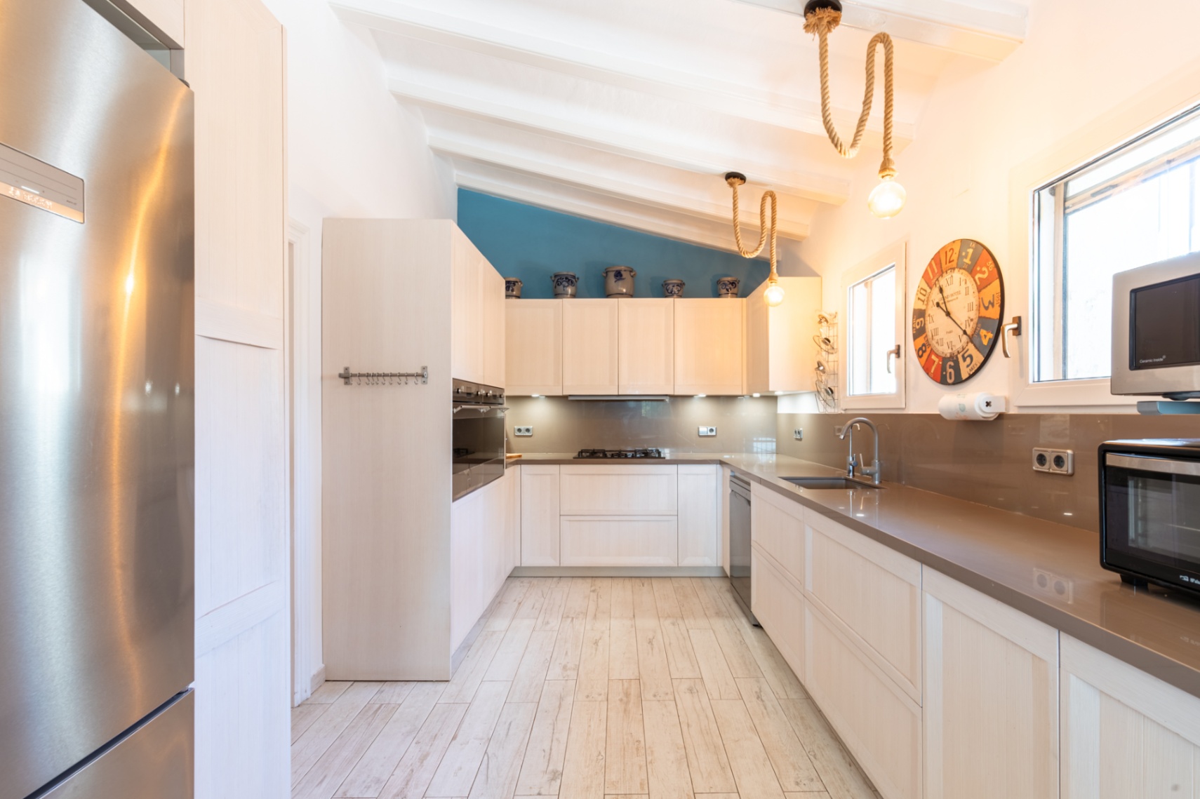 Fully equipped kitchen with stone countertops, stainless steel appliances, and a sloped beamed ceiling. Features decorative rope lighting and a blue accent wall.