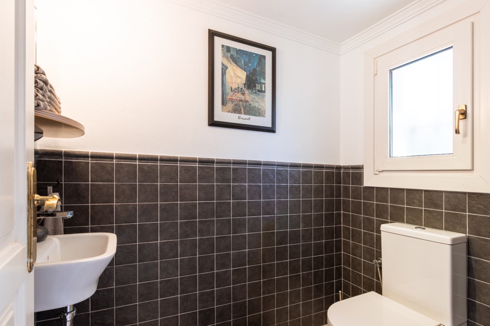 Functional guest toilet featuring dark textured wall tiles, a compact washbasin, and a tilt-and-turn window for natural ventilation.