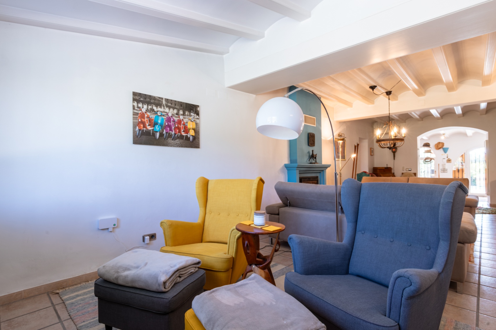 Living area featuring white beamed ceilings, a blue fireplace, and colorful wingback chairs illuminated by a contemporary arc floor lamp.