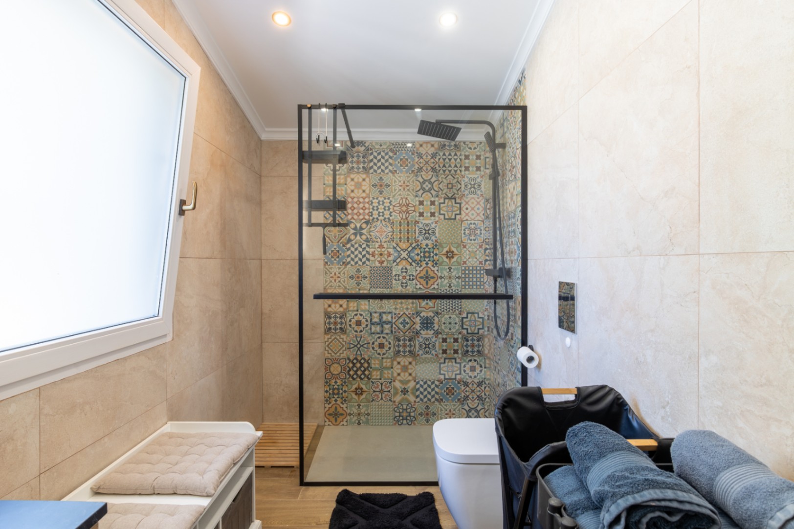 Modern bathroom featuring a walk-in shower with decorative patterned tiles, a black-framed glass screen, and neutral large-format wall tiling.
