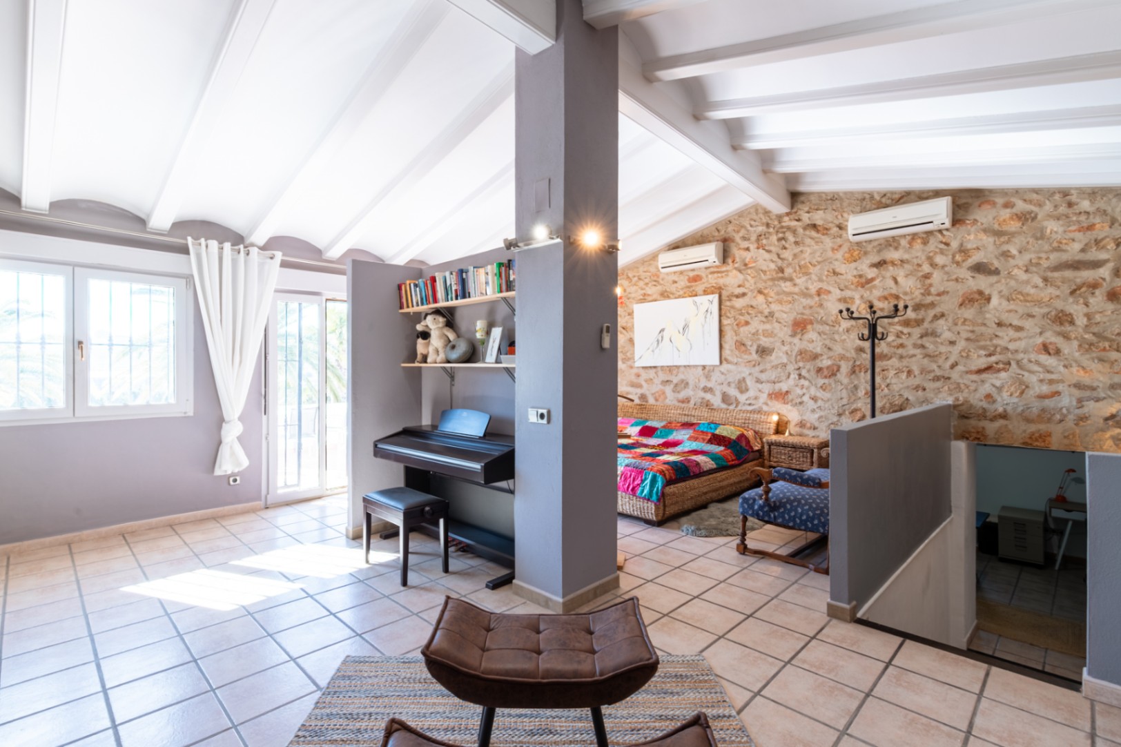 Open-plan upper floor featuring natural stone walls, white vaulted beam ceilings, and a dedicated piano area with terracotta tile flooring.
