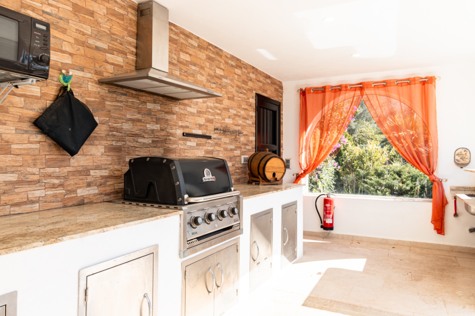 Outdoor kitchen featuring a built-in Broil King gas grill, granite countertops, and a natural stone accent wall with a professional stainless steel extractor.