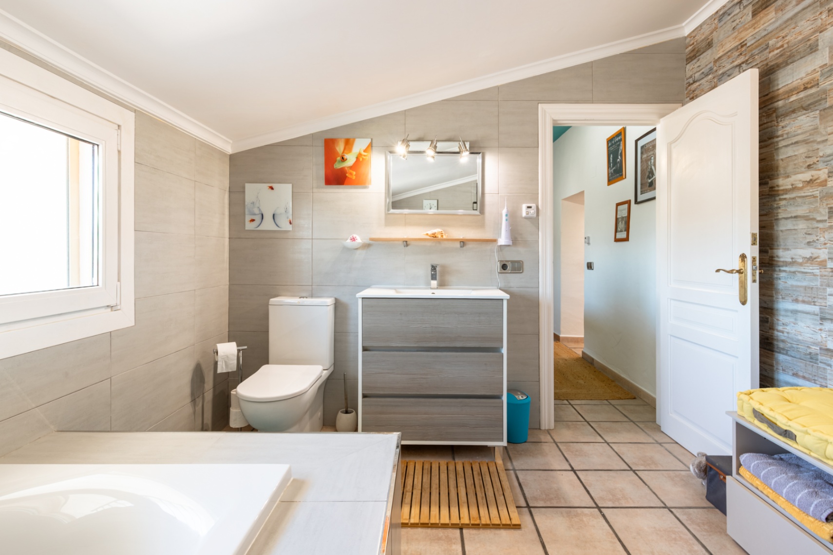 Renovated bathroom featuring a sloped ceiling, wood-effect vanity unit, and large-format wall tiles with a textured accent wall by the entrance.