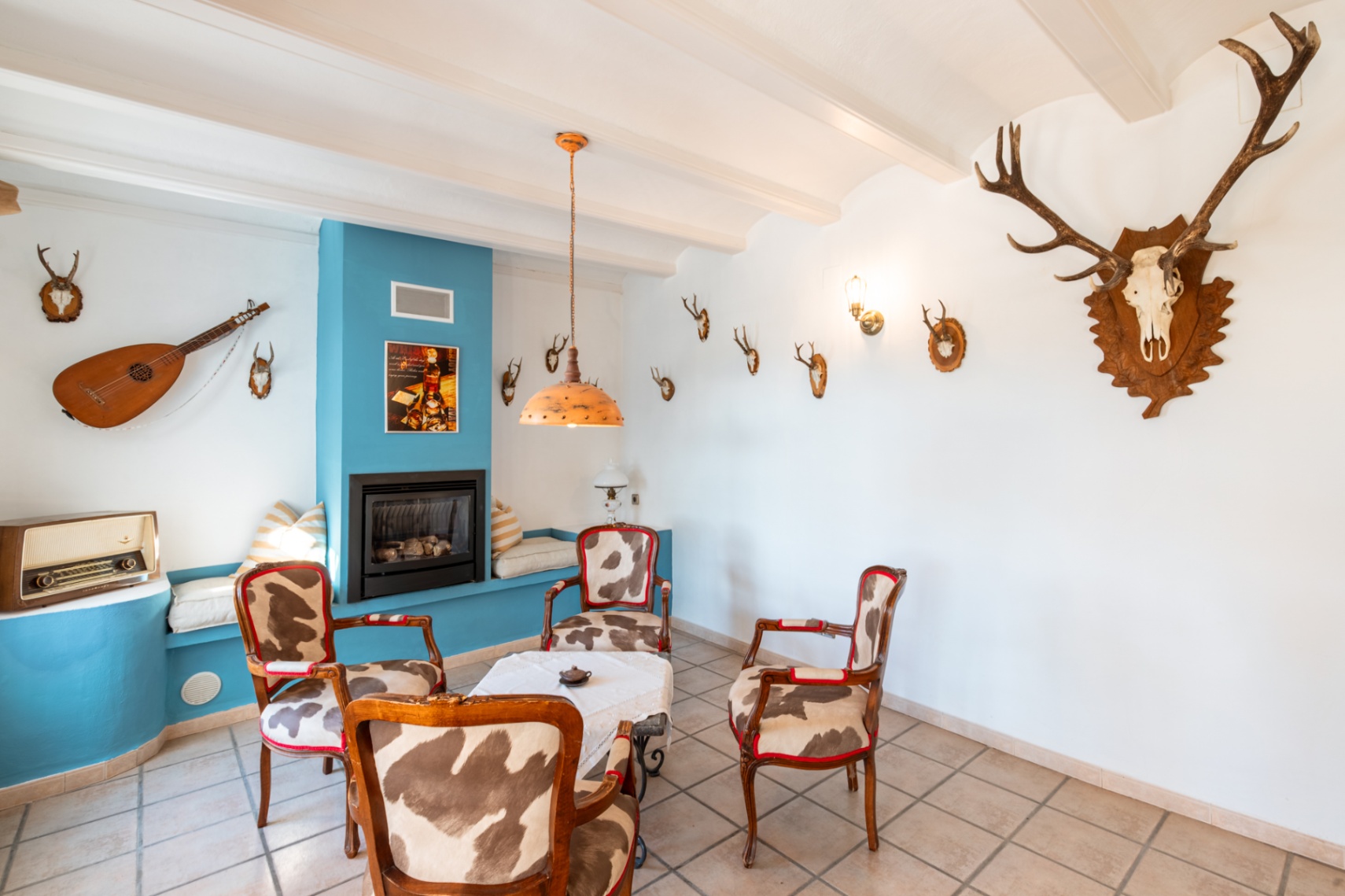 Rustic lounge featuring a gas fireplace in a blue accent wall, cowhide-upholstered armchairs, and traditional beamed ceilings with hunting-themed decor.