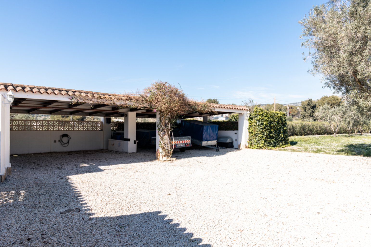 Spacious covered parking area with a traditional tiled roof and white pillars, set on a clean gravel driveway with capacity for multiple vehicles.