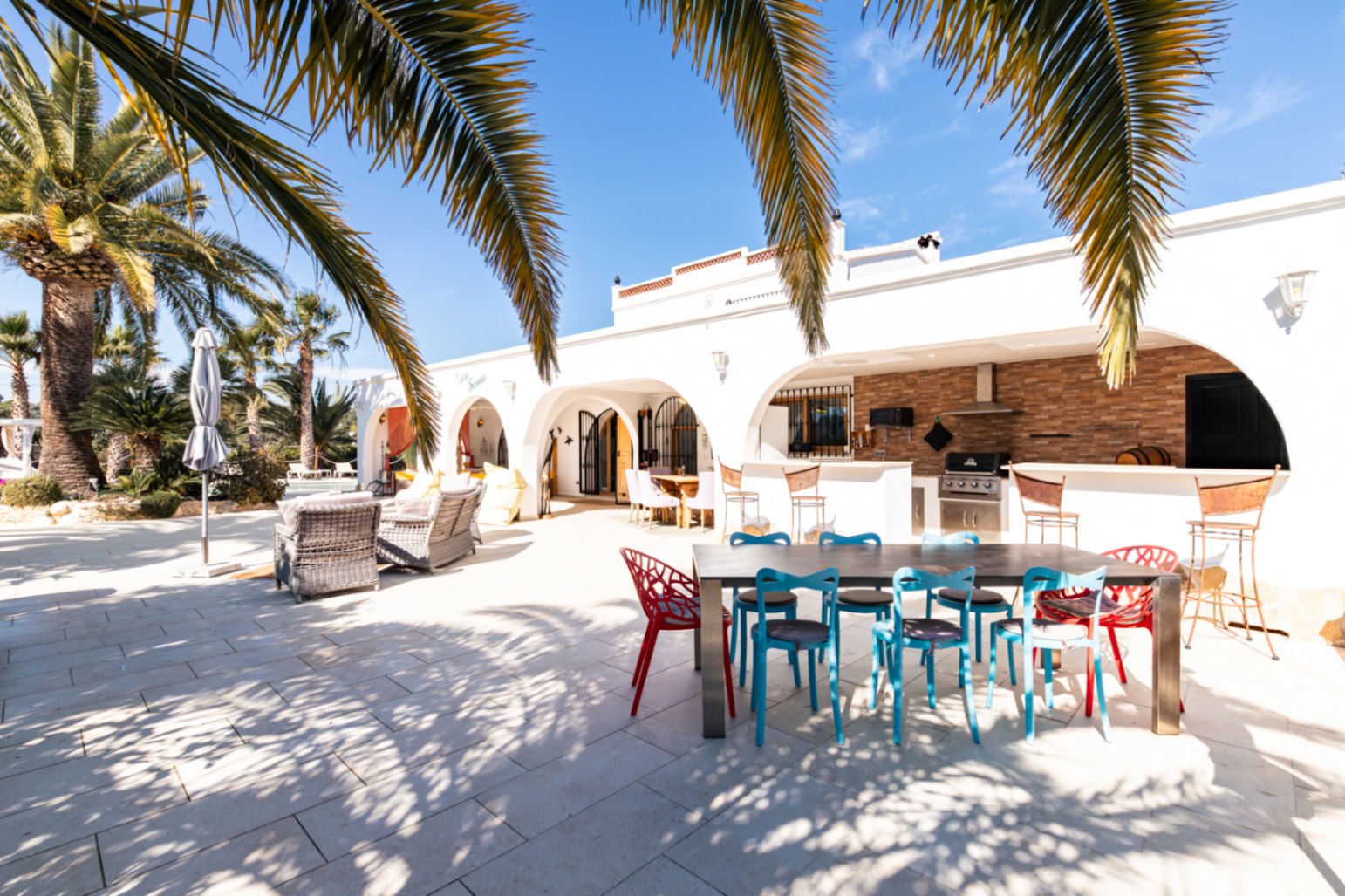 Spacious outdoor terrace featuring an arched naya, fully equipped summer kitchen with Broil King BBQ, and dining area surrounded by mature palms.