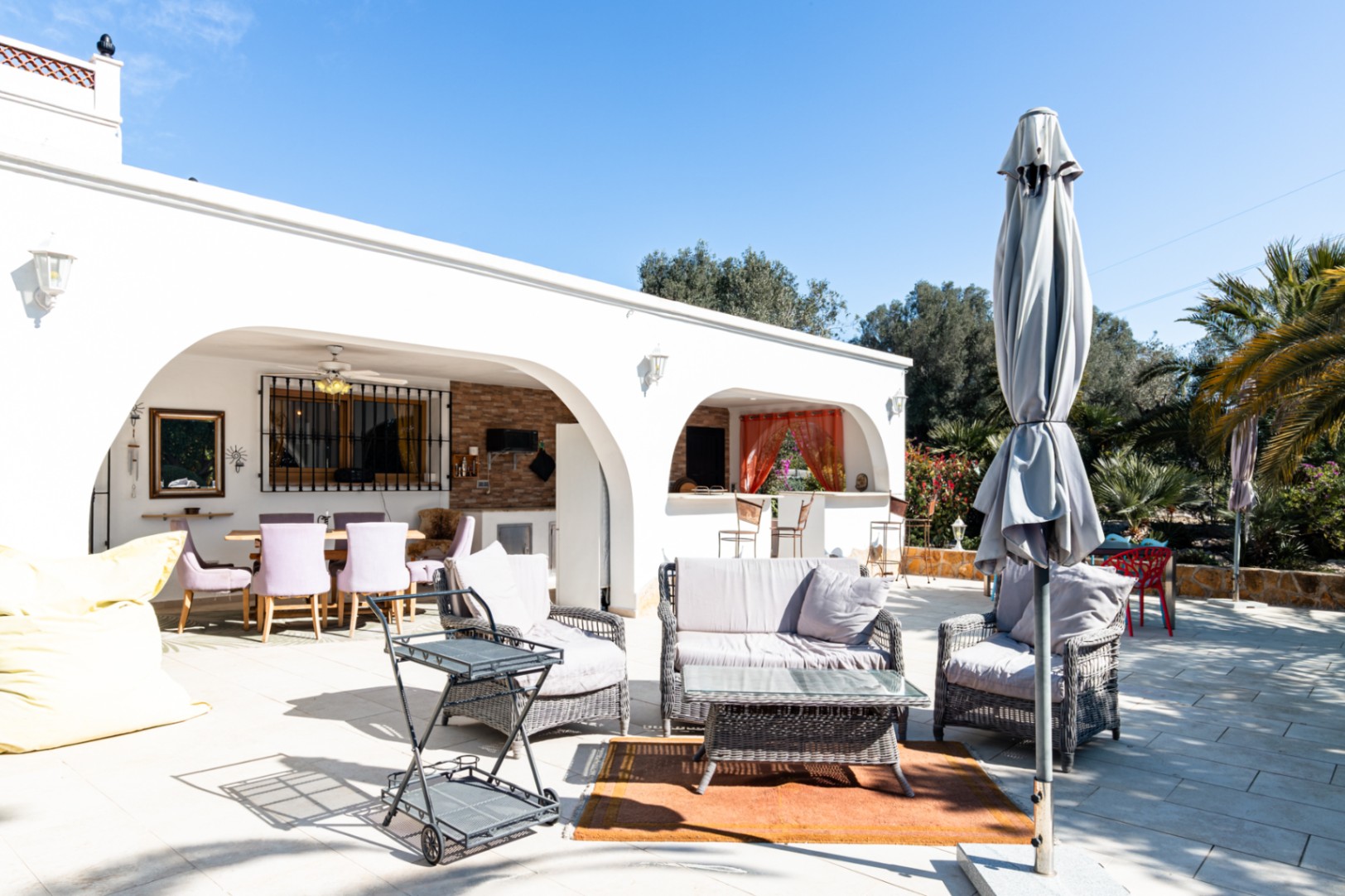 Spacious outdoor terrace featuring wicker lounge seating, a bar cart, and an arched naya with a dining area and integrated summer kitchen.
