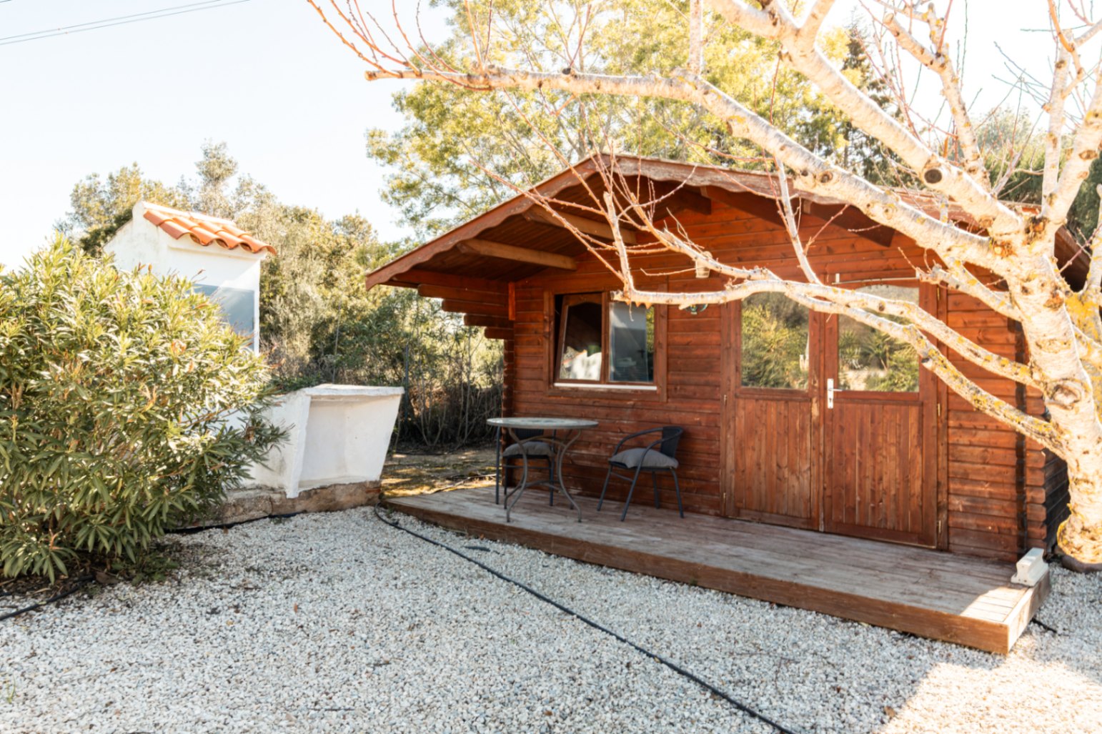 Wooden garden cabin featuring a small porch with seating, glass-paneled doors, and a gravel surround, providing versatile outdoor storage.