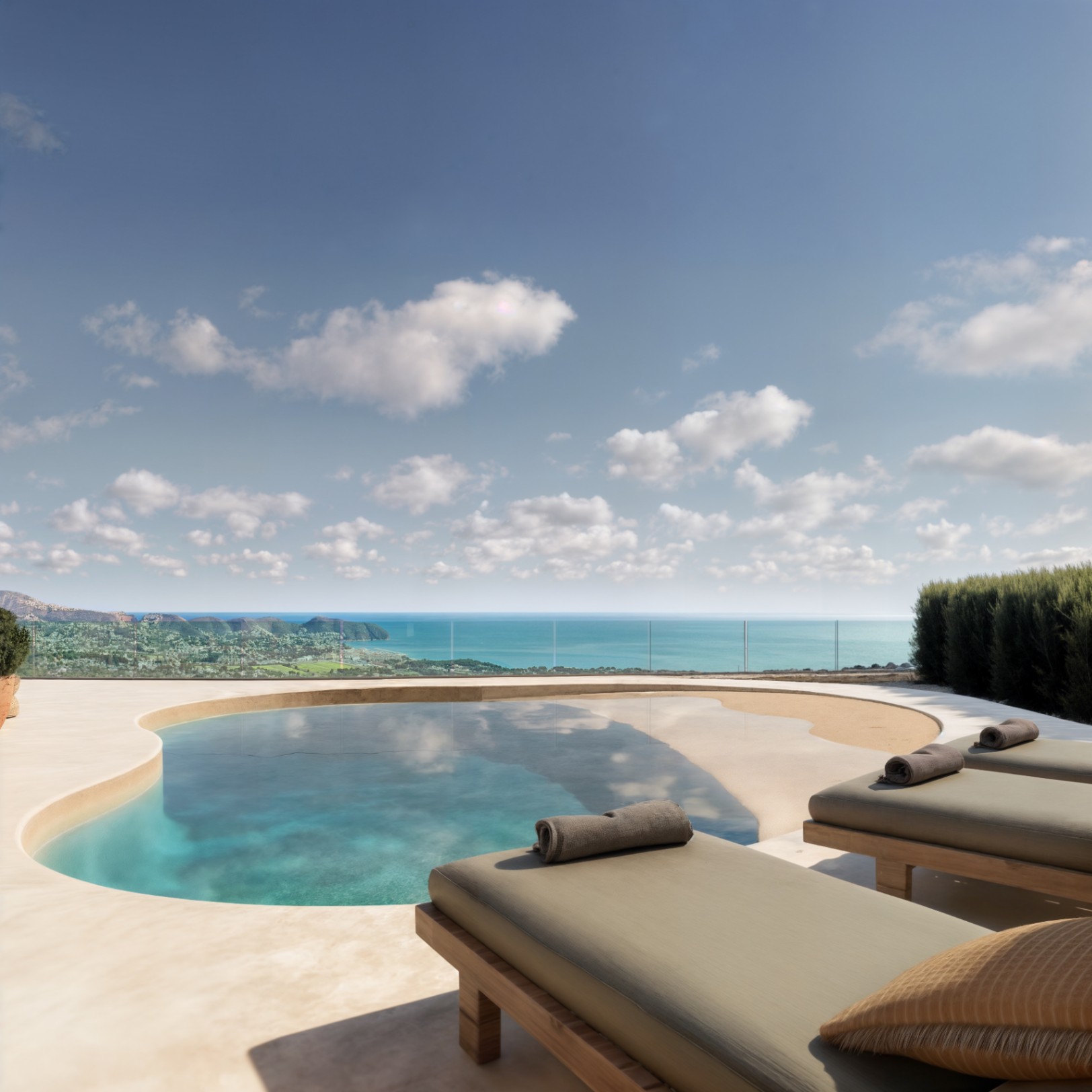 Outdoor terrace featuring an organic-shaped pool with beach entry, wooden sun loungers, and panoramic Mediterranean Sea views secured by glass balustrades.