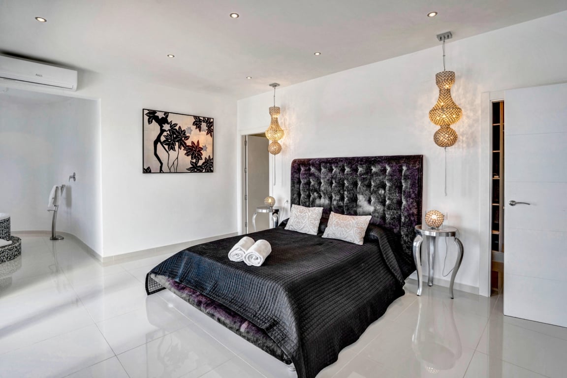 Bedroom featuring a tufted velvet headboard, polished porcelain tile floors, ornate pendant lighting, and wall-mounted air conditioning.