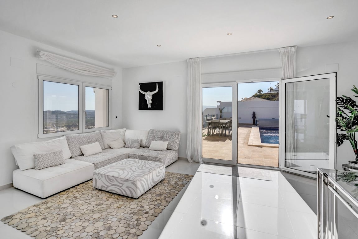 Bright living area featuring a modular sofa and direct access to the pool terrace through large glass doors with sea and mountain views.