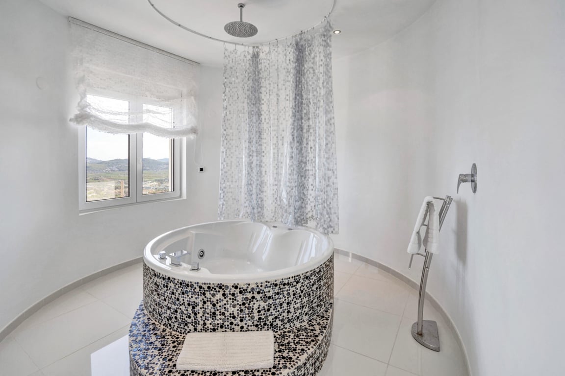 Designer bathroom with a circular hydromassage tub decorated with mosaics, an integrated rainfall shower, and a window with mountain views.