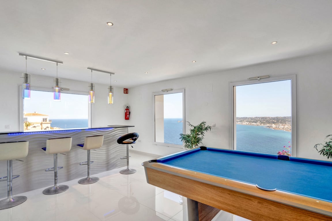 Entertainment room featuring a blue pool table and a modern bar with LED accents, overlooking the Mediterranean Sea through large windows.