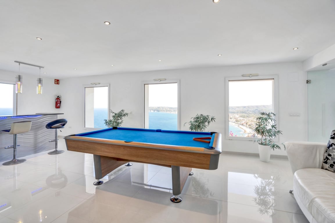Game room featuring a pool table, private bar area, and large windows offering panoramic views of the Mediterranean Sea and Javea coastline.