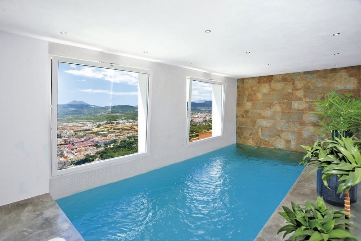 Indoor heated pool featuring large windows with panoramic mountain and valley views, complemented by a textured stone accent wall and recessed ceiling lighting.