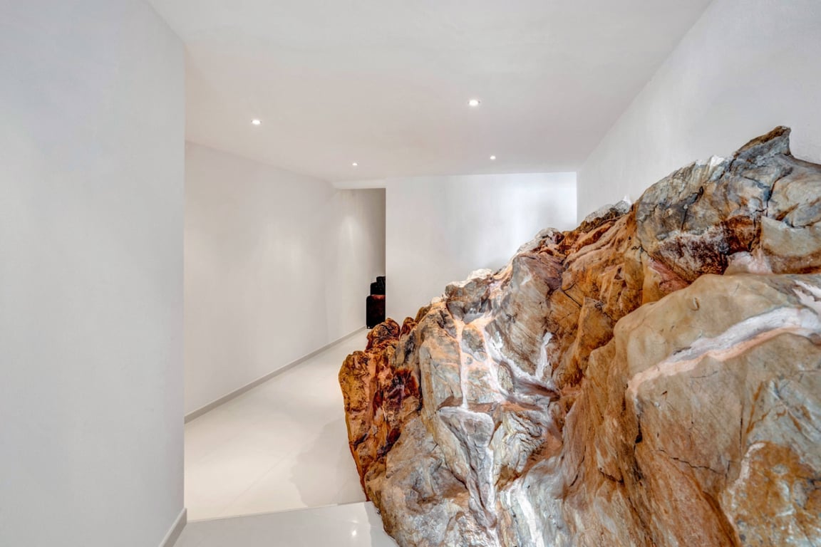 Interior hallway featuring a natural rock formation integrated into the architecture, minimalist white walls, and recessed ceiling lighting.