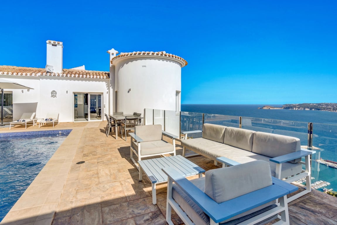 Main terrace featuring an outdoor lounge, dining area, and pool, with glass railings providing panoramic views of Jávea port and the Mediterranean Sea.
