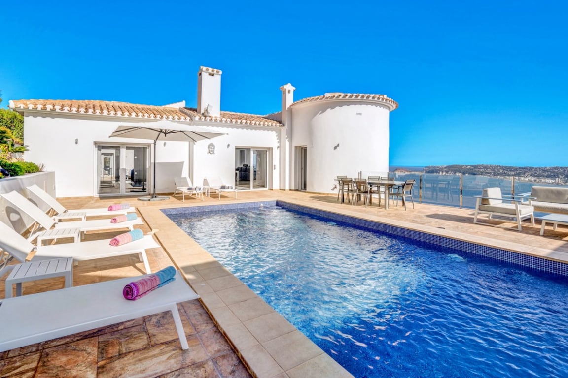 Main terrace featuring an outdoor swimming pool, sun loungers, and alfresco dining area overlooking the Mediterranean coast and Jávea harbor.