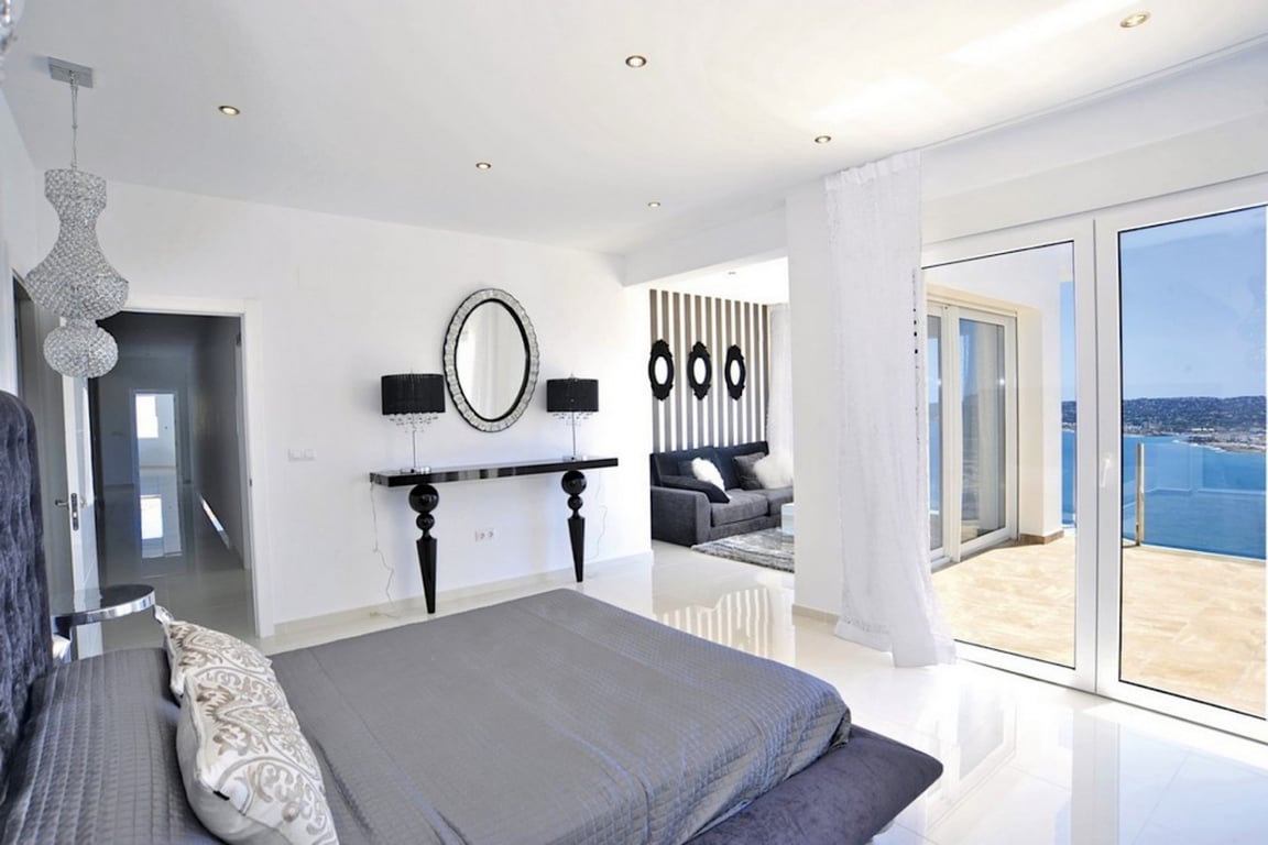 Master bedroom featuring white polished floors, an integrated lounge area, and large sliding doors opening to a terrace with expansive sea views.