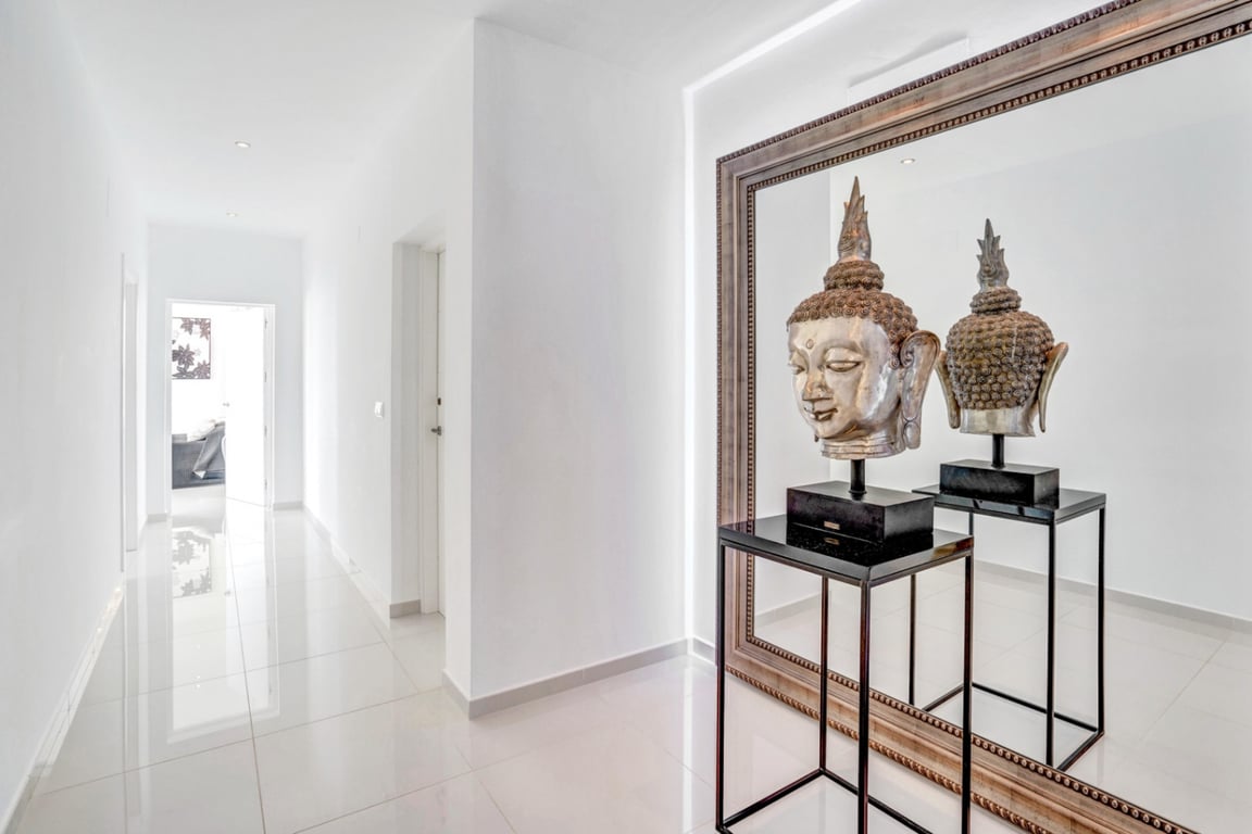Minimalist hallway featuring polished tile flooring and recessed lighting. A large framed mirror reflects a decorative silver Buddha head on a black pedestal.
