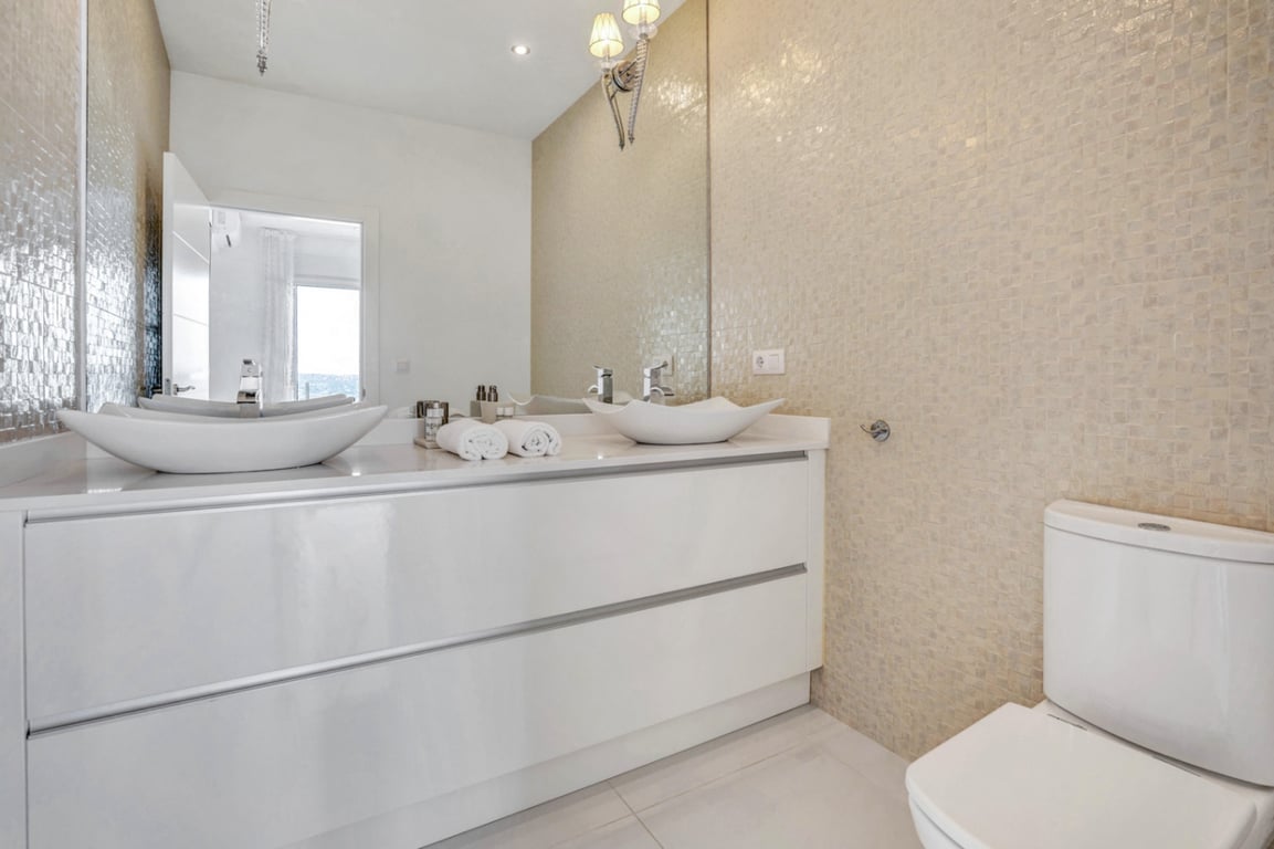 Modern bathroom featuring a double vanity with glossy white cabinetry, unique vessel sinks, and a textured beige mosaic tile wall.