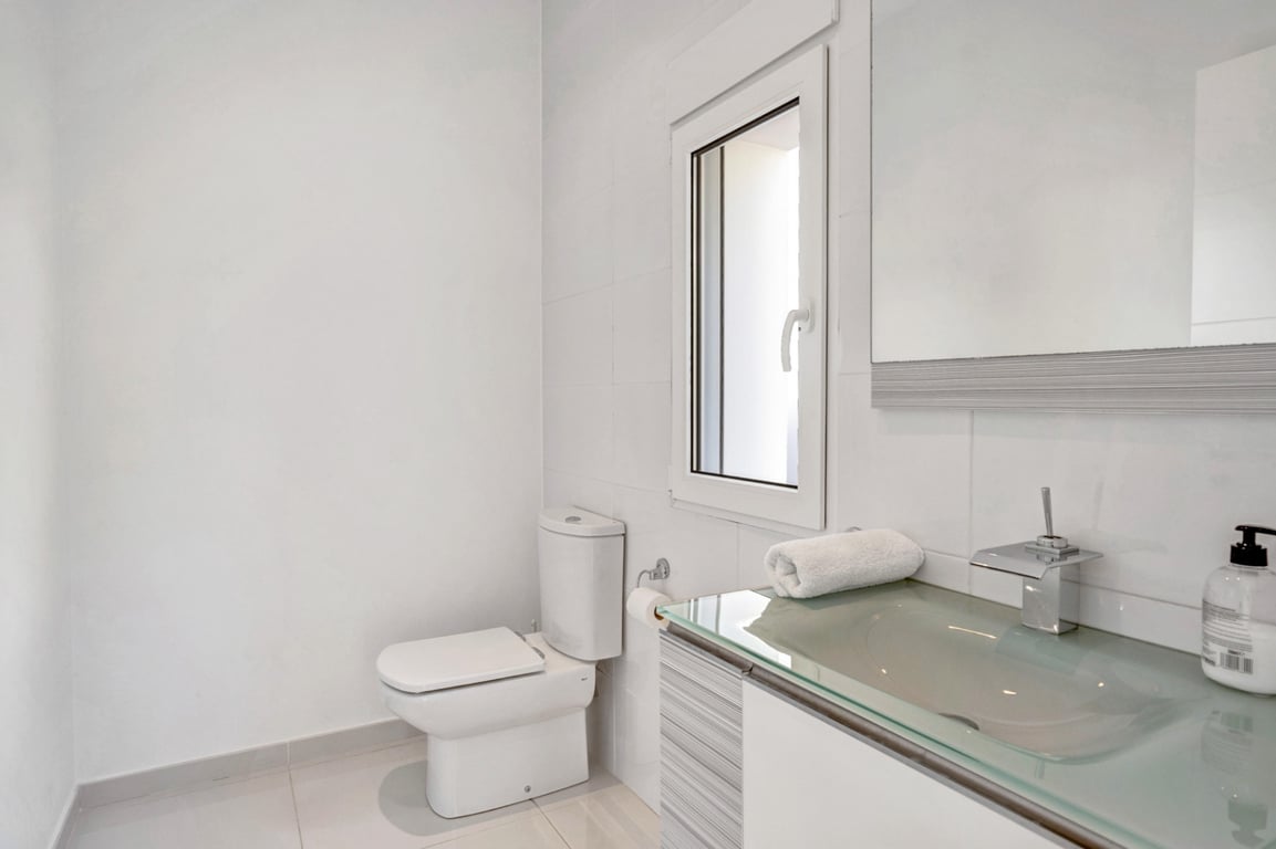 Modern bathroom featuring a translucent glass vanity top, chrome fixtures, and white tiled walls with a small functional window.