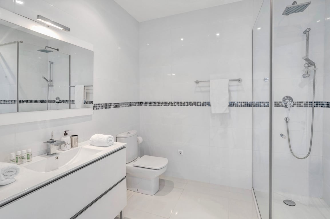 Modern bathroom featuring white tiling with a mosaic border, a sleek vanity unit, and a walk-in glass shower with chrome rain shower fixtures.