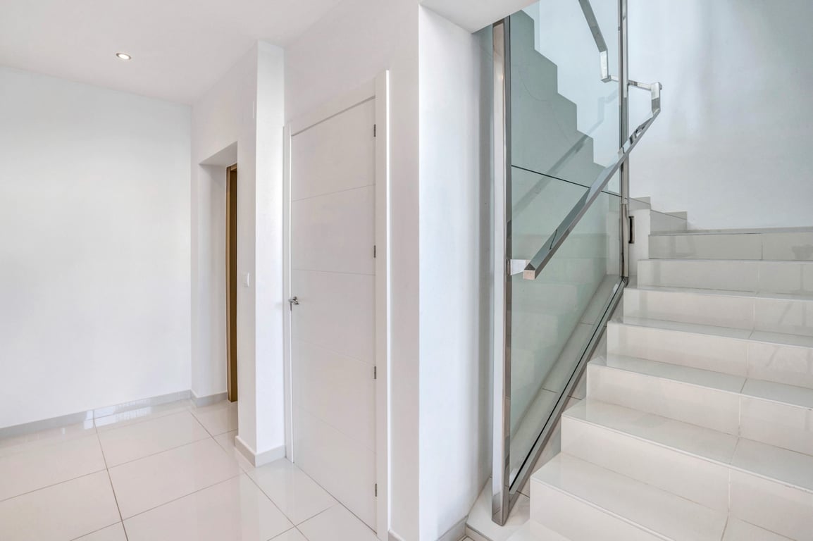 Modern interior hallway featuring white tiled flooring and a minimalist staircase with glass panels and stainless steel handrails.