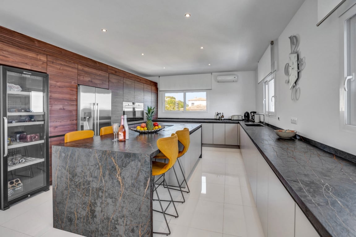 Modern kitchen featuring a dark stone island with waterfall edges, yellow bar stools, integrated appliances, and a dedicated wine cooler.