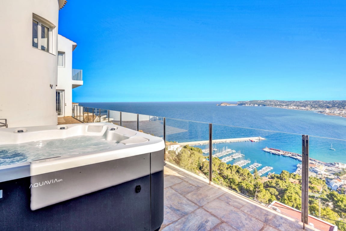 Outdoor Aquavia Spa jacuzzi on a stone-tiled terrace with glass railings, featuring panoramic views of Jávea port and the Mediterranean Sea.
