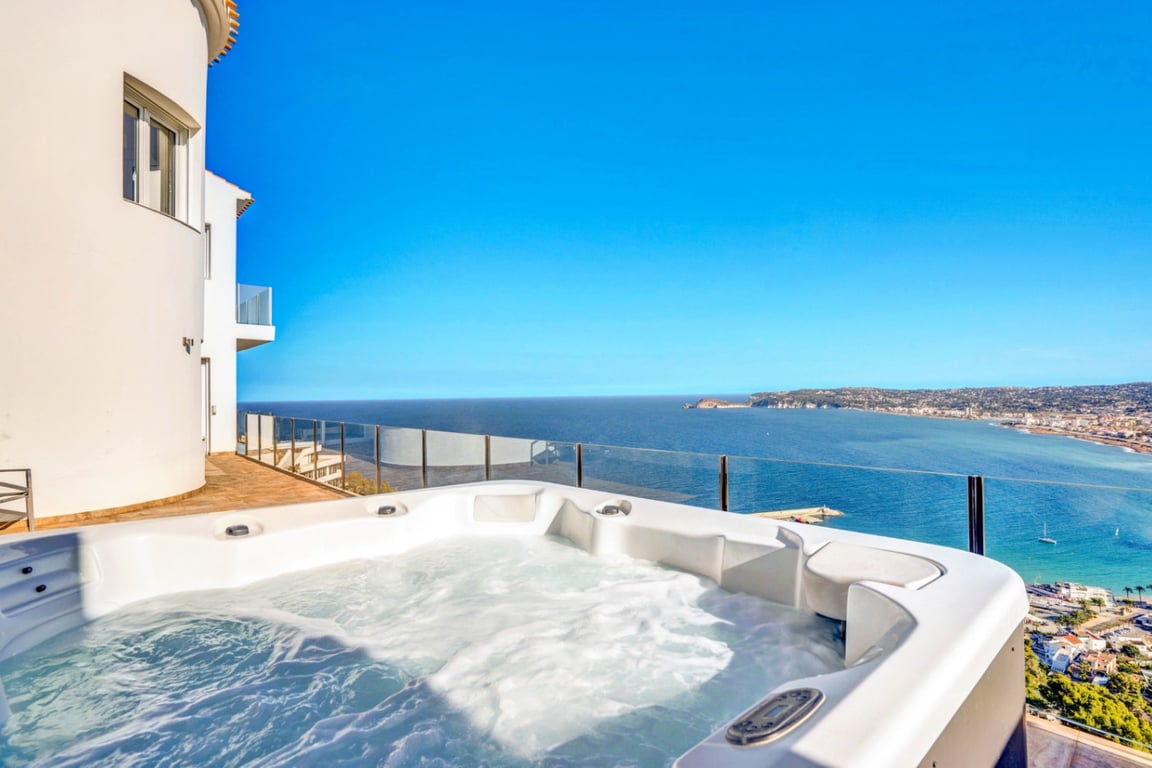 Outdoor jacuzzi on an elevated terrace with glass balustrades, featuring panoramic views of the Mediterranean Sea and Jávea bay.